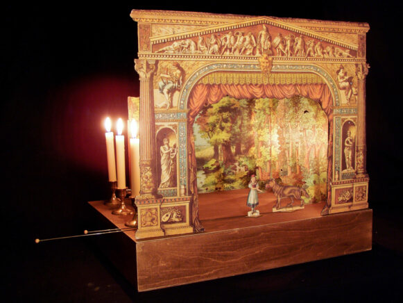 Un théâtre de papier avec les décors et les figurines du Petit Chaperon rouge, éclairé à la bougie.