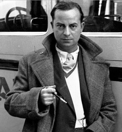 Un homme en manteau, tenant une cigarette à la main, regarde l'objectif