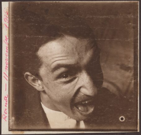 Autoportrait d'un homme, buste trois quart, faisant une grimace, la bouche ouverte, un oeil fixant l'objectif et l'autre caché dans l'ombre