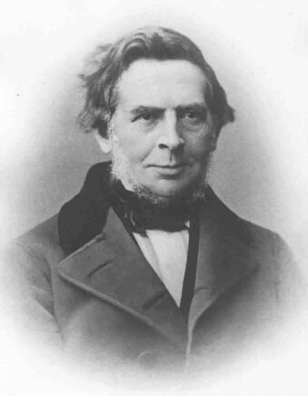 Portrait photographique d'un homme aux cheveux longs, portant un élégant manteau et un noeud papillon, le visage légèrement souriant.
