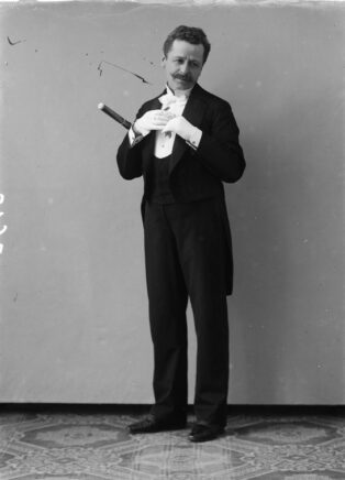 Photographie en pied de l'auteur, en costume et une flûte sous le bras