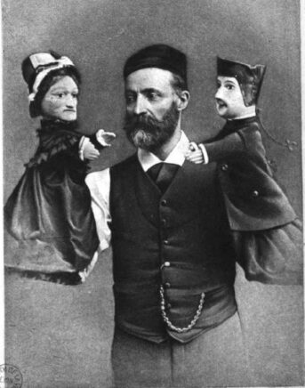 Le marionnettiste tient les deux marionnettes au bout de ses bras.