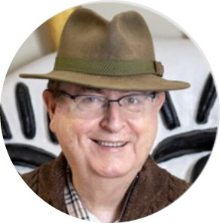 Photographie d'un homme souriant portant un chapeau Borsalino vert et des lunettes de vue.