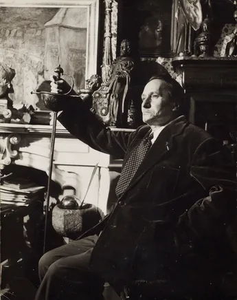 Photographie d'un homme assis tenant à la main une grande épée ancienne.