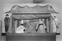 Photographie d'un castelet où l'on voit au milieu les marionnettes de Pulcinella, avec un masque noir et un chapeau long blanc, et Teresina, bien plus grande que Pulcinella et portant une robe longue.