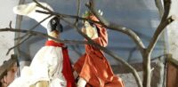 Deux marionnettes à gaine, représentant Pulcinella et Dante Alighieri, sont derrière une branche d'un arbre, sur la scène d'un castelet