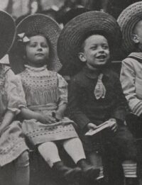 Deux enfants, une petite fille et un petit garçon assis côte à côte, suivent le spectacle de marionnettes d'un air ébahi.