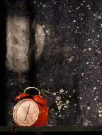 Photographie d'un reveil rouge ancien devant un drap recouvert de tâches de peinture.