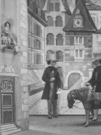 Photographie d'un spectacle avec des petits personnages, au centre de se trouve un homme avec un chapeau haut-de-forme, à gauche une femme à sa fenêtre et à droite un homme tirant des ânes.