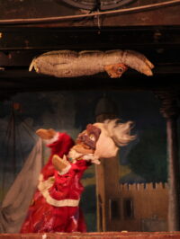 Une photographie d'un spectacle de Gigio Brunello où le diable regarde le lapin Ginetto suspendu au dessus du castelet.