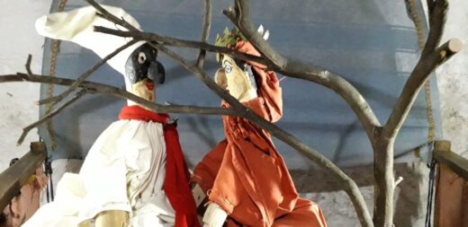 Deux marionnettes à gaine, représentant Pulcinella et Dante Alighieri, sont derrière une branche d'un arbre, sur la scène d'un castelet