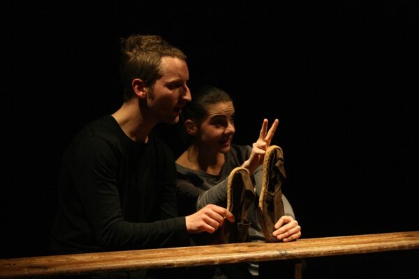 Photographie de spectacle où l'on voit un homme et une femme manipuler chacun une espadrille.