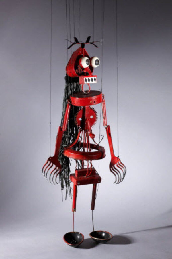 Photo d'une marionnette à fils représentant un personnage composé de morceaux de métal avec des grands yeux.