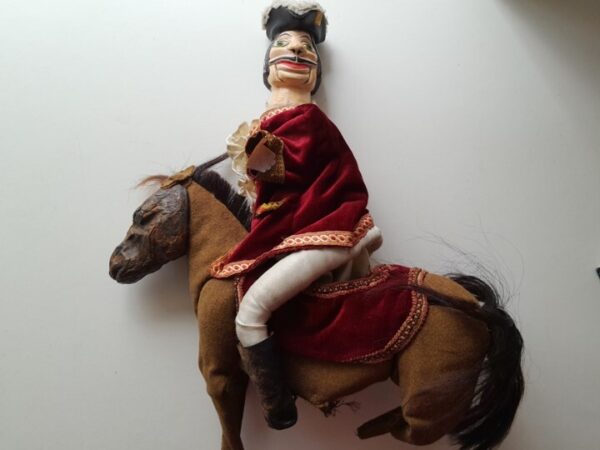 Une marionnette représentant un homme avec une large moustache, un tricorne et un beau costume sur un cheval.